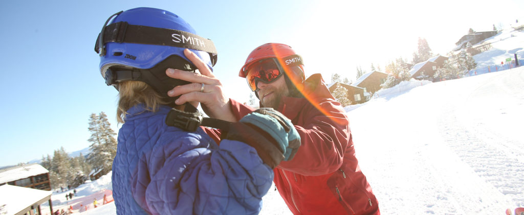 Photo of ski instructor fitting a helmet onto a child's head.